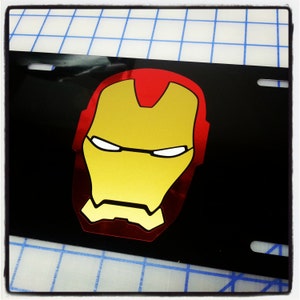 May include: A black license plate with a red and gold Iron Man mask design.