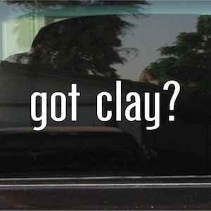 May include: A white vinyl decal with the text "got clay?" on a black car window.