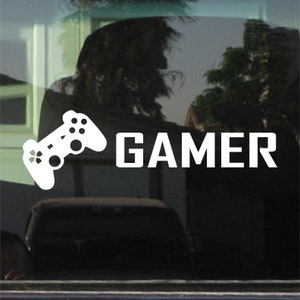 Könnte beinhalten: Weißer Vinyl-Aufkleber mit einem Videospiel-Controller und dem Wort "GAMER" auf schwarzem Hintergrund.