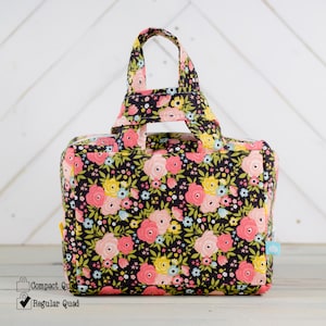 May include: A floral print tote bag with a black background, featuring pink, yellow, and blue flowers. The bag has a rectangular shape with a top handle and a zipper closure. The bag is made of fabric and has a small tag on the side.