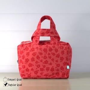 May include: A red floral-patterned tote bag with a rectangular shape and a top handle. The bag features a repeating pattern of small flowers in a darker shade of red. The bag has a white zipper and a small tag on the side.