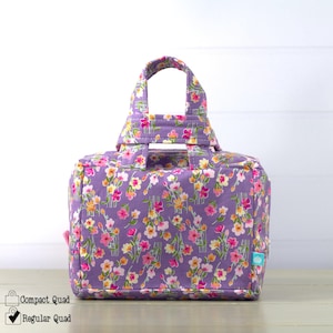 May include: A floral print tote bag in shades of purple, pink, yellow, and green. The bag has a handle and a rectangular shape. The text on the image says "Compact Quad" and "Regular Quad".