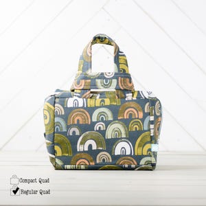 May include: A small, gray fabric tote bag with a rainbow pattern. The bag has a single top handle and a zipper closure.