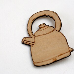 Puede incluir: Un recorte de madera de una tetera marrón con asa y pico. La tetera es un diseño simple sin detalles adicionales.
