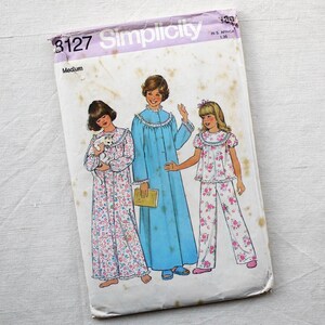 May include: Vintage Simplicity sewing pattern 8127 showing illustrations of three sleepwear designs. The pattern cover depicts a long blue robe, a long floral nightgown, and a floral pajama set. The pattern is for a medium size.