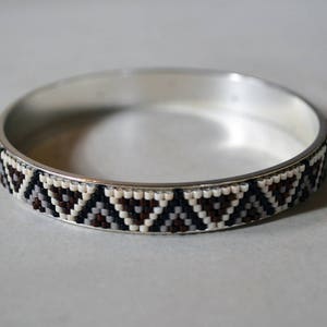 May include: A silver bangle bracelet with a geometric pattern of black, white, and brown beads.