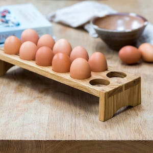 May include: A wooden egg holder with 10 brown eggs in it. The holder is made of light brown wood and has a rectangular shape. It is sitting on a wooden table.