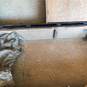 May include: The inside of a vintage suitcase with a floral patterned lining. The suitcase is open and the lining is visible. There is a piece of fabric in the bottom of the suitcase.