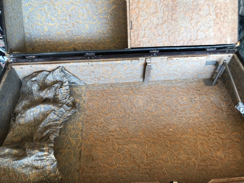 May include: The inside of a vintage suitcase with a floral patterned lining. The suitcase is open and the lining is visible. There is a piece of fabric in the bottom of the suitcase.