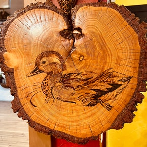 May include: A wooden slice with a detailed burned image of a duck. The wood has a natural grain pattern and a brown color.