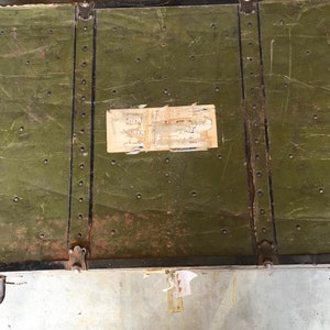 Puede incluir: Un ba&uacute;l vintage de metal verde con detalles en metal negro y una etiqueta en la parte superior.