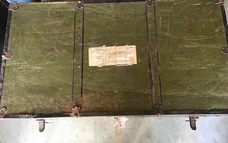 Puede incluir: Un ba&uacute;l vintage de metal verde con detalles en metal negro y una etiqueta en la parte superior.