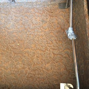May include: The inside of a vintage suitcase with a brown floral patterned lining. A metal luggage rack is attached to the side of the suitcase.