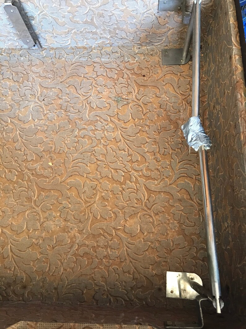 May include: The inside of a vintage suitcase with a brown floral patterned lining. A metal luggage rack is attached to the side of the suitcase.