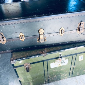 May include: Two vintage green metal suitcases with brass hardware and rivets. The top suitcase has a label that says "Sterling".