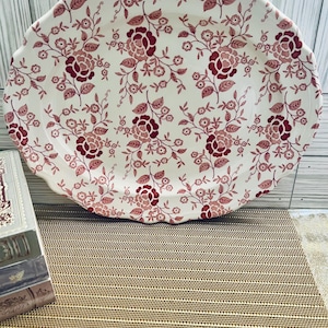 May include: A white oval serving platter with a red floral pattern. The platter has a scalloped edge and is made of ceramic.