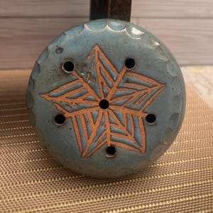 May include: A blue ceramic wheel with a brown star design and holes around the edge. The wheel is sitting on a brown woven mat.
