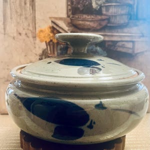 May include: A ceramic pot with a lid, featuring a blue and white abstract design. The pot is sitting on a wooden stand.