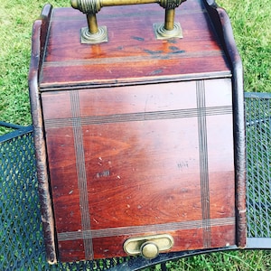 May include: A wooden boot box with a brass handle and a brass latch. The box has a dark wood finish and is decorated with a grid pattern.