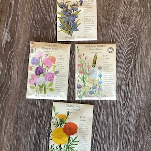 May include: Four seed packets for flowers, each with a different variety and color. The packets are labeled with the flower name, 'Forget-Me-Not Victoria Blue', 'Sweet Pea Bouquet Blend', 'Bachelor Button Dwarf Blend', and 'Marigold Giant Sunset'. Each packet includes information about the flower, such as its growing habits, bloom time, and sun requirements.