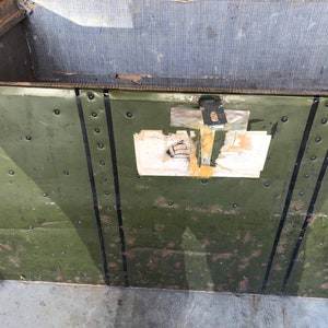 Puede incluir: Un ba&uacute;l vintage de metal verde con rayas negras pintadas y remaches. El ba&uacute;l tiene un cierre de metal y una etiqueta con el texto "72 224".