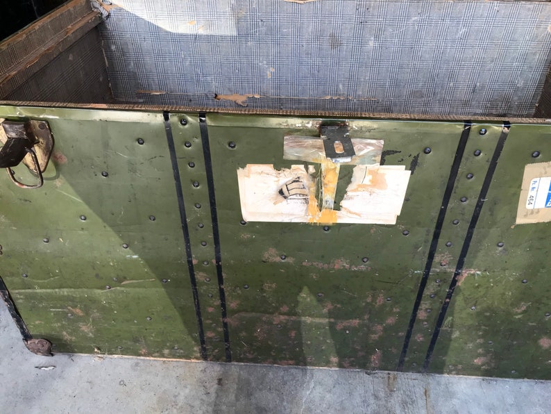 Puede incluir: Un ba&uacute;l vintage de metal verde con rayas negras pintadas y remaches. El ba&uacute;l tiene un cierre de metal y una etiqueta con el texto "72 224".