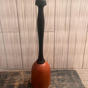 May include: A wooden mallet with a black handle and a red-brown head. The mallet is sitting on a dark wooden surface.
