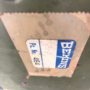 Puede incluir: Primer plano de una etiqueta blanca con texto azul que dice "Siemens" y "Pc. No. 464" sobre una superficie verde.