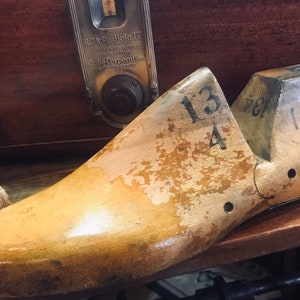 May include: A wooden shoe last with the numbers "13 4" and "1133XX" written on it. The last is a light brown color and has a worn, weathered appearance.