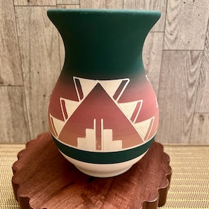 May include: A green, red, and white ceramic vase with a geometric pattern. The vase is sitting on a wooden base.