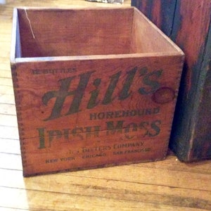 May include: A vintage wooden box with a brown stain and black lettering. The box is labeled "Hill's Horehound Irish Moss" and "Butters Company, New York, Chicago, San Francisco".