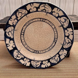 May include: A white ceramic plate with a blue and white design of rabbits and floral patterns. The plate has a crackled glaze and a raised rim.