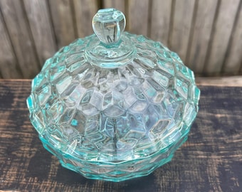 Op de afbeelding: Een heldere, lichtblauwe glazen snoepkom met een koepelvormig deksel en een diamantpatroon. De kom staat op een donker houten oppervlak.