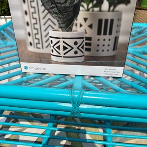 May include: A Silhouette brand vinyl starter kit with a white ceramic planter with a black geometric design. The kit includes vinyl for crafting.