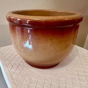 May include: A large, round, terracotta planter with a brown glaze. The planter has a smooth, slightly textured surface and a wide, rounded rim.