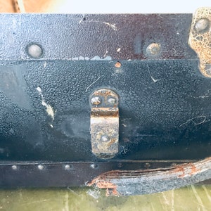 May include: Close-up of a black vintage suitcase with a metal latch and a leather strap. The suitcase has a textured surface and shows signs of wear and tear.