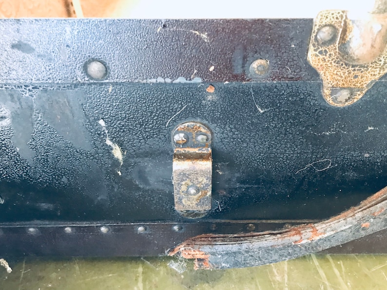 May include: Close-up of a black vintage suitcase with a metal latch and a leather strap. The suitcase has a textured surface and shows signs of wear and tear.