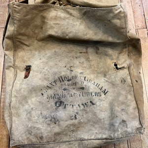 May include: A vintage canvas bag with a brown leather strap and the text "Grant Holden Graham Limited Manufacturers Ottawa" printed on the front.