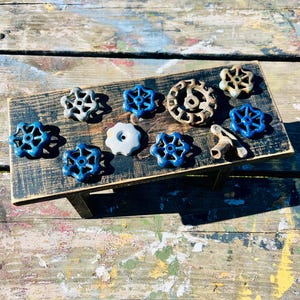 May include: A collection of blue and gray metal knobs with a rusty gear on a black wooden surface.
