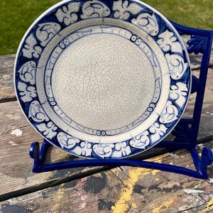 May include: A white ceramic plate with a blue and white floral design. The plate has a crackled glaze and is displayed on a blue metal stand.