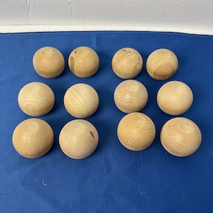 May include: Twelve wooden balls, all the same size and shape, are arranged in a semi-circle on a blue surface. The balls are a light brown color and have a smooth, slightly textured surface.
