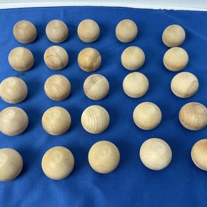 May include: A collection of 25 natural wood balls, each with a smooth, round surface. The balls are arranged in a grid pattern on a blue fabric background.