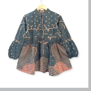 May include: A green and brown patterned blouse with a button-up front and long sleeves. The blouse has a gathered waist and a slightly flared hem.