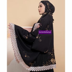 May include: Black prayer shawl with gold floral embroidery and white lace trim. The shawl has a hood and is worn by a person.