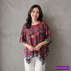 May include: A red batik top with a black and white floral pattern. The top has a round neckline and short sleeves with a black and white border. The model is wearing a gold pendant necklace and white pants. The text "kononkatanya" is in the bottom right corner.