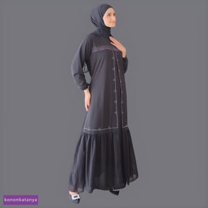 May include: A black abaya with a ruffled hem and delicate embroidery. The embroidery features a pattern of small white flowers and silver beads.