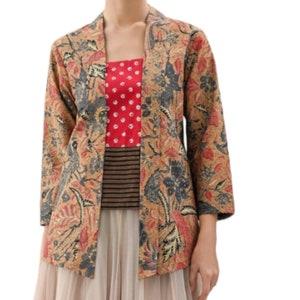 Puede incluir: Chaqueta beige de frente abierto con un estampado floral en rojo, azul y gris. La chaqueta se lleva sobre una camiseta roja con lunares blancos y una camiseta a rayas. El conjunto se completa con una falda beige.