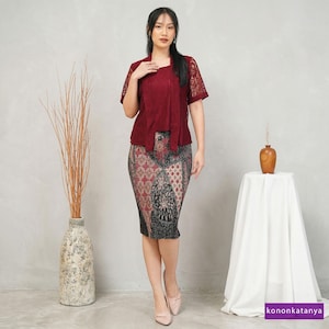 Peut inclure: Un ensemble composé d'un haut en dentelle bordeaux à manches courtes et d'une jupe crayon assortie. La jupe présente un motif rouge, noir et gris. La tenue est portée avec des talons roses clairs. L'image comprend un vase avec des branches sèches et une petite table.