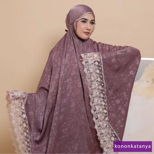 May include: A mauve prayer shawl with a floral pattern and white lace trim. The shawl is draped over a person's shoulders.
