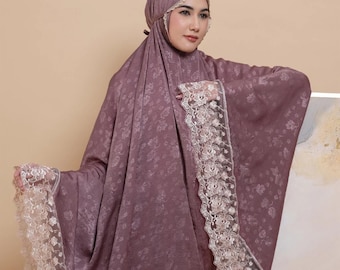 May include: A mauve prayer shawl with a floral pattern and white lace trim. The shawl is draped over a person's shoulders.